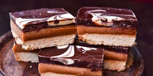 A stack of chocolate and caramel shortbread biscuits, sitting on a dark wooden board