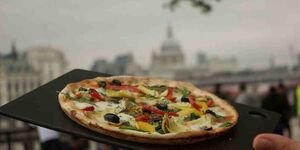 A close-up of a pizza with the London skyline in the background