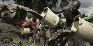 Image of a man pouring water from a bucket over mud.