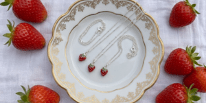Three silver nacklaces with strawberry pendants on a plate