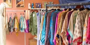 A photograph of the inside of a shop. Brightly-coloured clothing hangs from rails