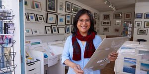 Image of an artist holding a print while stood in the gallery.