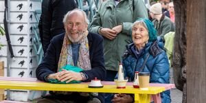 A woman and a man sit at a yellow wooden picnic bench, smiling