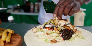 A person puts vegetables into a tortilla wrap. Only their hand is visible.