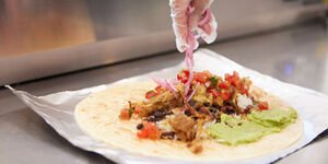 A photograph of a tortilla being filled with guacamole, salad and meat