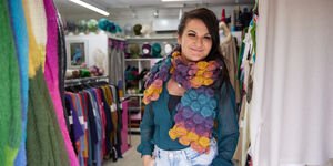 A woman stands in a shop wearing a ,ulticoloured knitted scarf