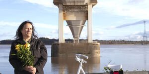 Image of a woman holding flowers by a bridge.