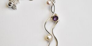 An image of a silver necklace with pearls and purple jewels.