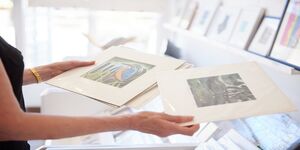 A person holds two prints in their hands, only the arms and hands are visible 