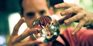 A man is looking at a crystal ball floating between his hands. His face is reflected in the ball 