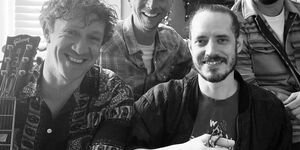 A black and white photograph or four men, seated. They are smiling at the camera.