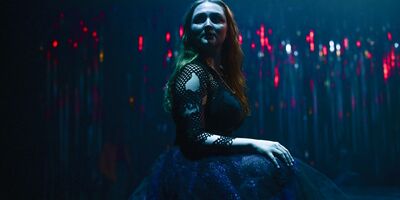 Image of a woman in a black dress sitting on stage.