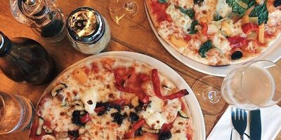 Image of two pizzas surrounded by drinks.