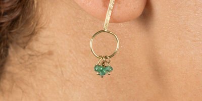 Image of a woman modelling gold emerald earrings.