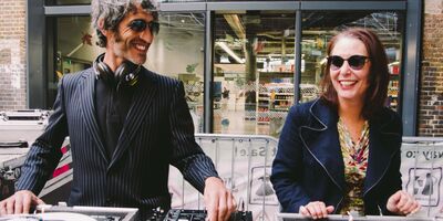A man and a woman stand smiling in front of some turntables