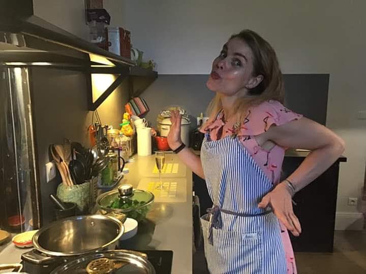 Andrea, hand on hip, smiling next to a stove cooking