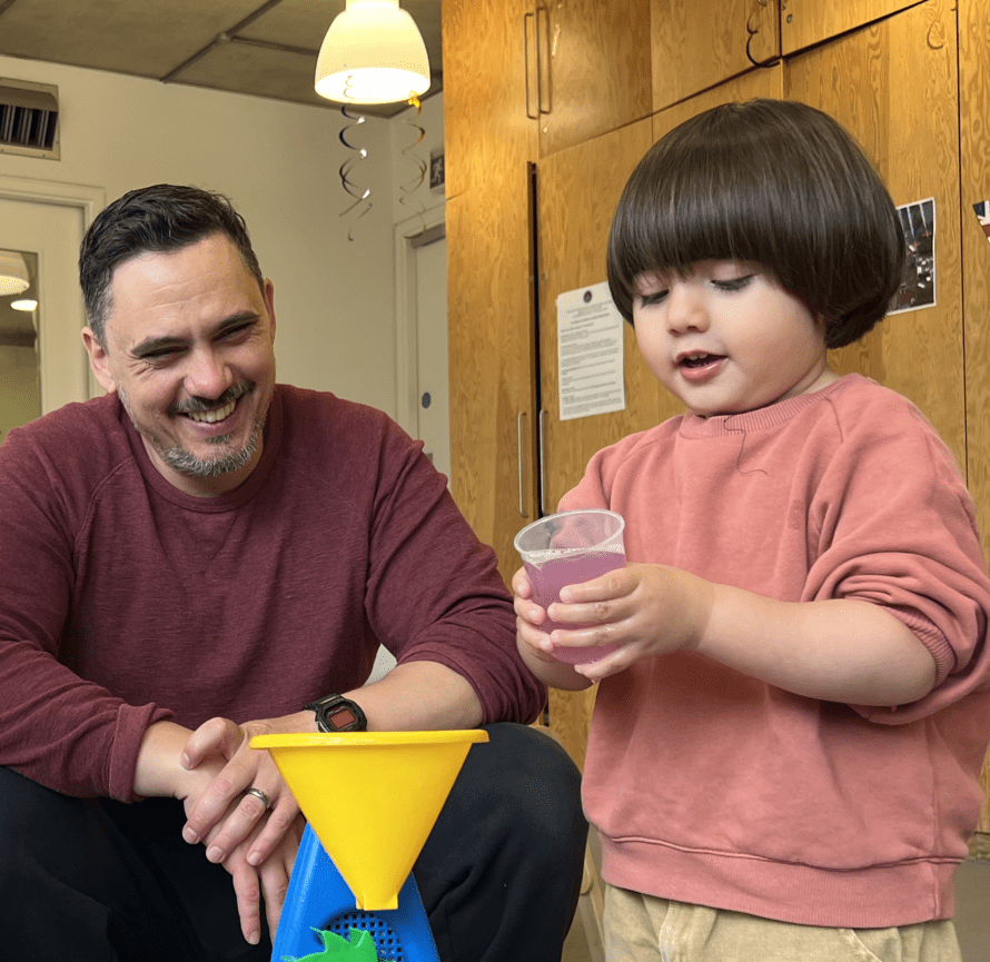 Dad smiles at his son who is playing with a toy