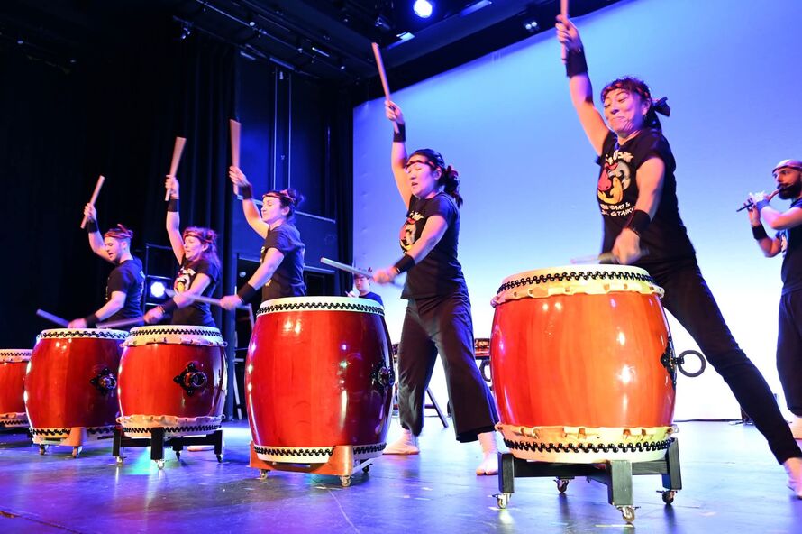 A group of 5 people dressed in black stand in front of large red drums