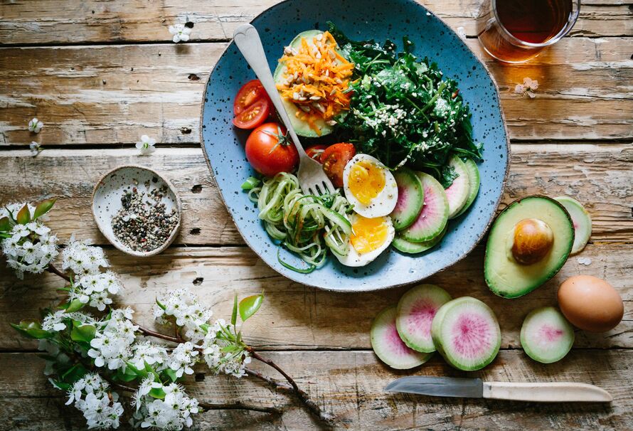 Image of a salad surrounded by other vegetables on a wooden table.