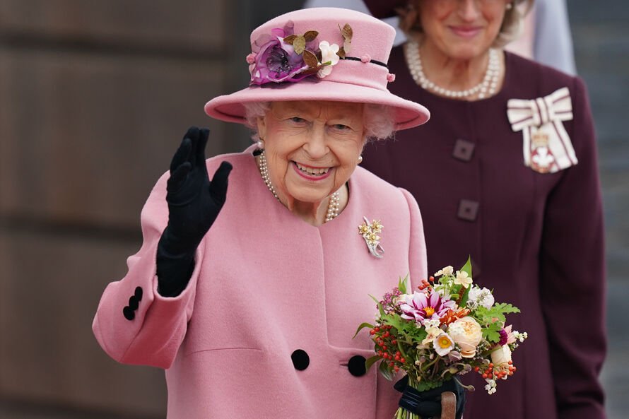Picture of The Queen wearing a pink coat and hat, holding flowers